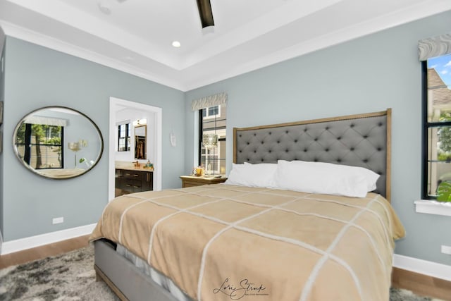 bedroom featuring a tray ceiling, hardwood / wood-style floors, ceiling fan, and ensuite bath