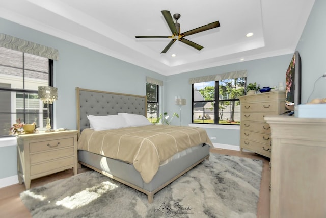 bedroom with a raised ceiling, light wood-type flooring, and ceiling fan