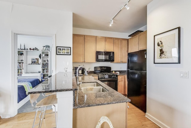 kitchen featuring light wood finished floors, a sink, black appliances, dark stone countertops, and a kitchen breakfast bar