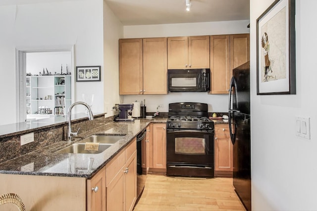 kitchen with a peninsula, a sink, light wood-type flooring, black appliances, and dark stone countertops