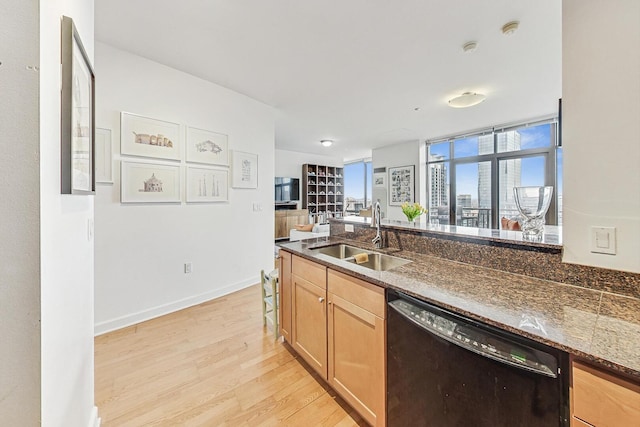 kitchen featuring black dishwasher, baseboards, light wood-style flooring, dark stone countertops, and a sink