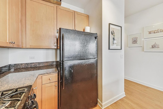 kitchen featuring light wood-style flooring, baseboards, freestanding refrigerator, dark stone counters, and gas stove