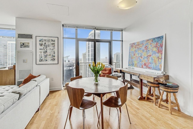 dining room with a view of city, light wood-type flooring, visible vents, and floor to ceiling windows