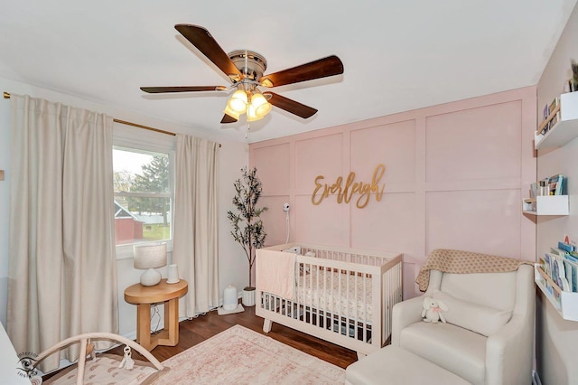 bedroom with a crib, dark hardwood / wood-style floors, and ceiling fan