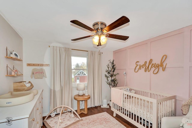 bedroom with a nursery area, dark hardwood / wood-style floors, and ceiling fan