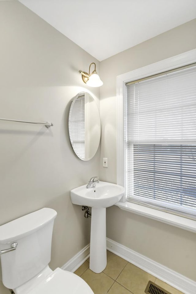 half bath with visible vents, baseboards, toilet, tile patterned flooring, and a sink