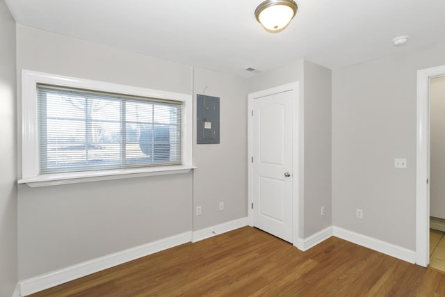 unfurnished bedroom with wood finished floors, electric panel, and baseboards