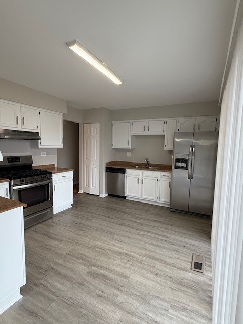 kitchen with appliances with stainless steel finishes, sink, white cabinets, and light hardwood / wood-style floors