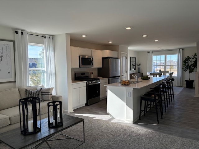 kitchen featuring white cabinets, appliances with stainless steel finishes, open floor plan, a kitchen breakfast bar, and a kitchen island with sink