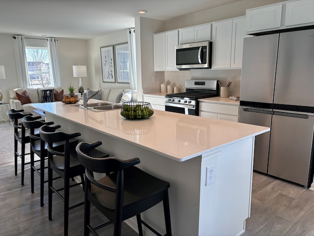 kitchen featuring open floor plan, appliances with stainless steel finishes, a center island with sink, and white cabinets