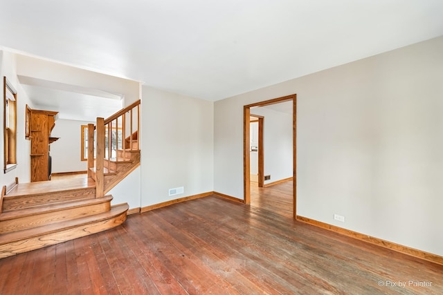 unfurnished living room featuring baseboards, visible vents, stairway, and dark wood-style flooring