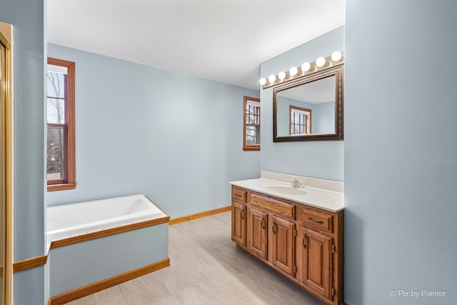 bathroom featuring vanity, baseboards, and a bath