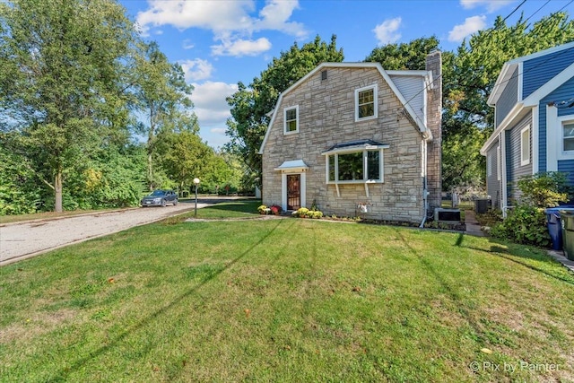 view of front of property with a chimney, a gambrel roof, cooling unit, stone siding, and a front lawn