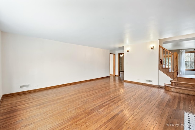 unfurnished living room with light wood finished floors, baseboards, stairs, and visible vents