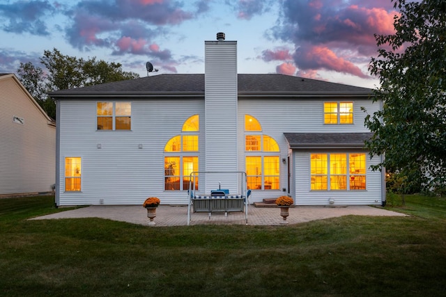 back house at dusk featuring a yard and a patio