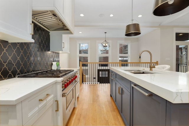 kitchen with white cabinetry, stainless steel range, an island with sink, custom range hood, and decorative light fixtures