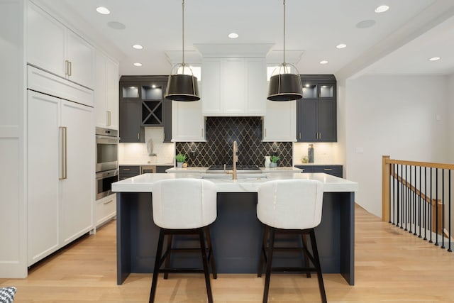 kitchen with an island with sink, appliances with stainless steel finishes, white cabinets, and decorative light fixtures