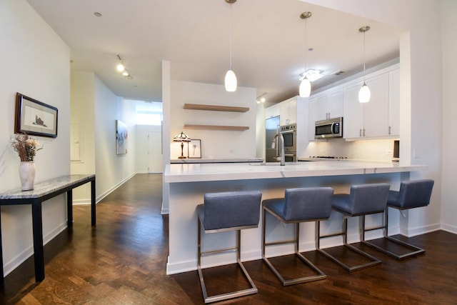 kitchen featuring a breakfast bar area, white cabinets, backsplash, hanging light fixtures, and dark wood-type flooring