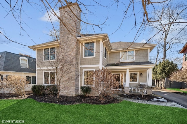 view of front of home featuring covered porch, a shingled roof, a chimney, and a front yard