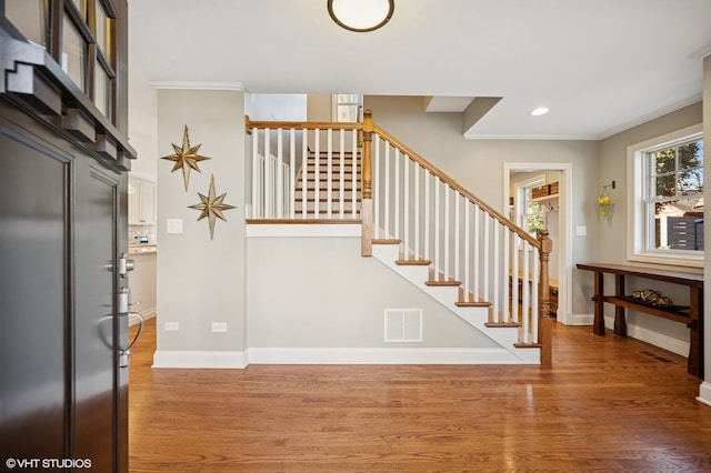 stairs with ornamental molding, visible vents, baseboards, and wood finished floors