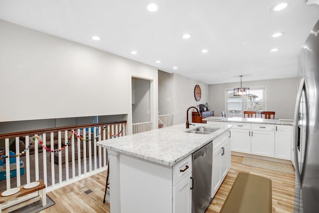 kitchen featuring appliances with stainless steel finishes, an island with sink, sink, hanging light fixtures, and light wood-type flooring