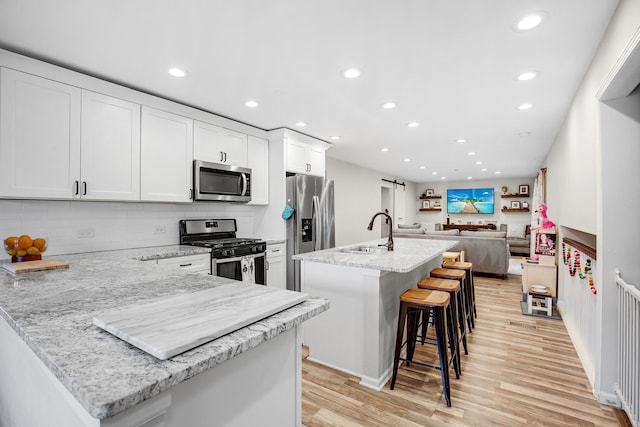 kitchen featuring white cabinetry, a breakfast bar area, stainless steel appliances, and an island with sink