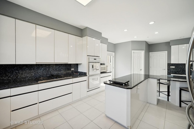 kitchen featuring dark stone countertops, white appliances, a center island, and white cabinets