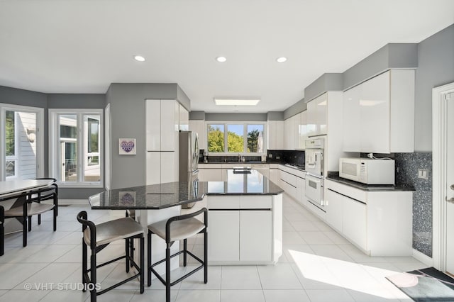 kitchen featuring tasteful backsplash, white appliances, white cabinets, and a kitchen bar