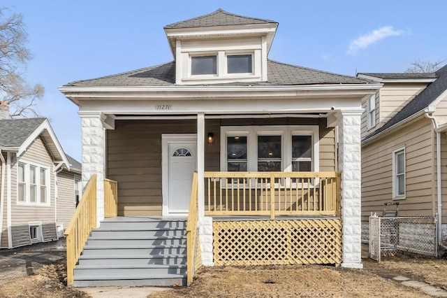 view of front of home with a shingled roof, covered porch, and fence