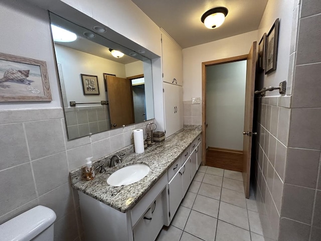 half bathroom featuring toilet, tile patterned flooring, tile walls, and vanity