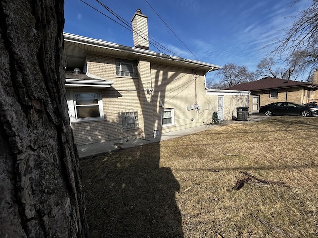 back of house with a chimney, a lawn, and brick siding