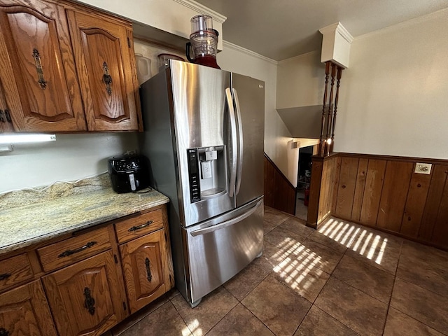 kitchen with wooden walls, stainless steel fridge with ice dispenser, a wainscoted wall, light stone counters, and crown molding