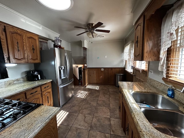 kitchen featuring light stone counters, stainless steel refrigerator with ice dispenser, wainscoting, a sink, and wooden walls