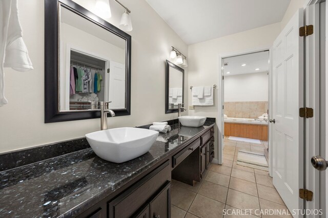 bathroom with tile patterned flooring, double vanity, a bath, and a sink