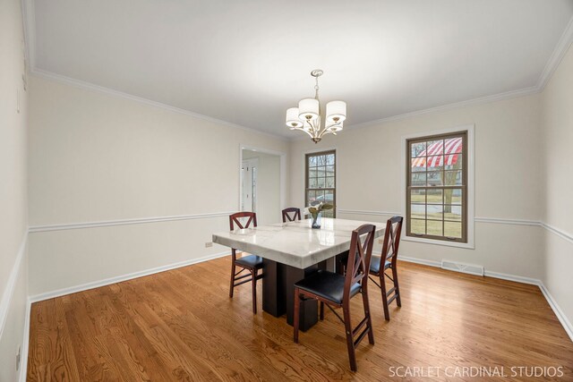 dining room with light wood-type flooring, visible vents, ornamental molding, an inviting chandelier, and baseboards