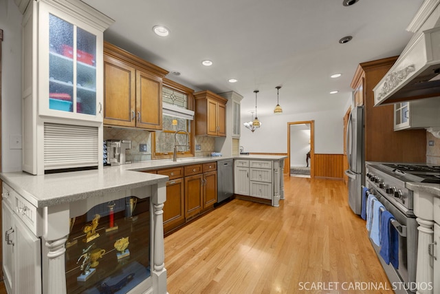kitchen featuring premium range hood, a wainscoted wall, a peninsula, brown cabinetry, and stainless steel appliances