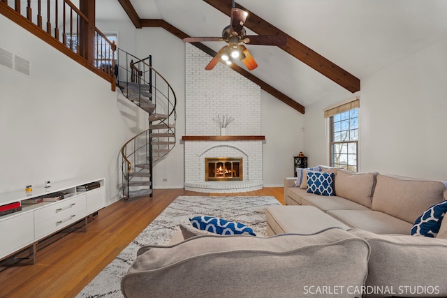living room with stairway, wood finished floors, visible vents, high vaulted ceiling, and a fireplace