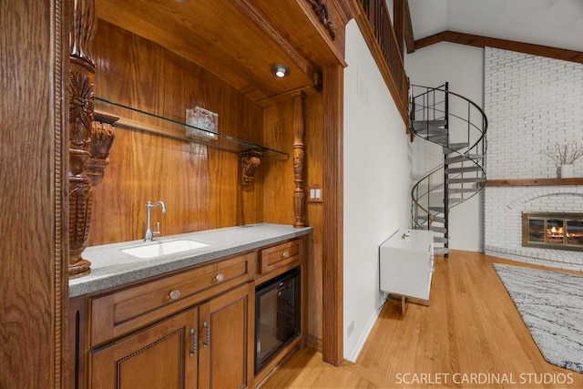 interior space with a brick fireplace, stairway, vaulted ceiling, light wood-style floors, and a sink