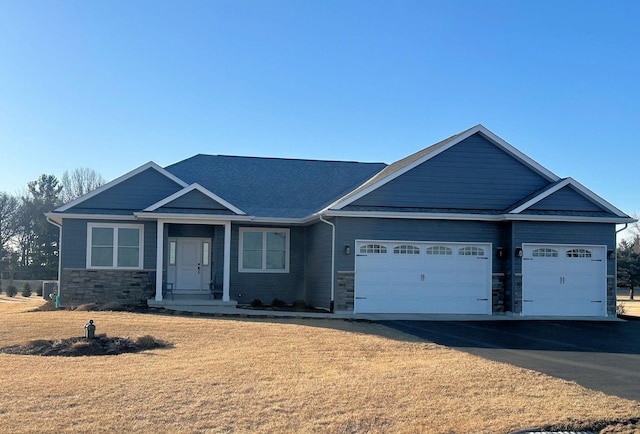 craftsman house with a front lawn, a garage, stone siding, and driveway