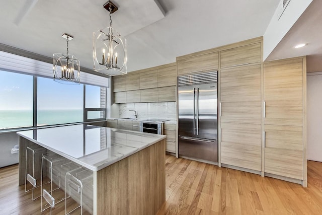 kitchen with a water view, built in refrigerator, decorative light fixtures, a center island, and light hardwood / wood-style floors