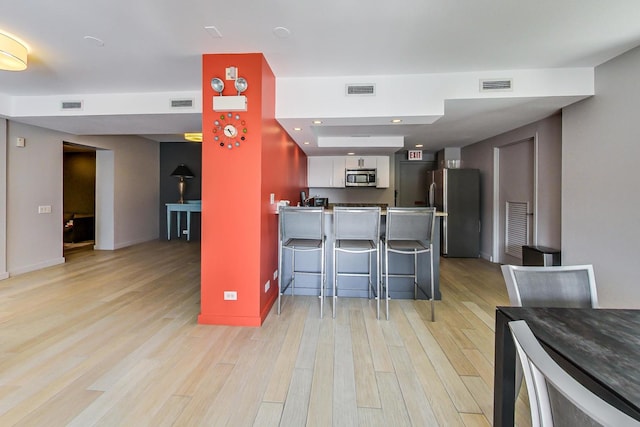 kitchen featuring light hardwood / wood-style flooring, appliances with stainless steel finishes, a kitchen breakfast bar, white cabinets, and kitchen peninsula