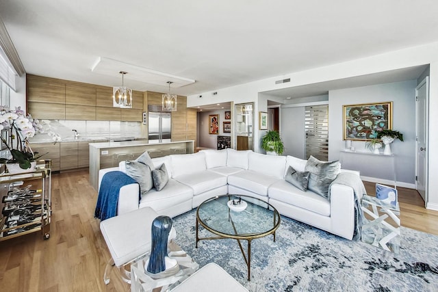 living room featuring an inviting chandelier, sink, and light wood-type flooring