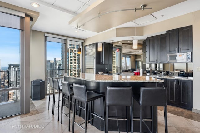 kitchen featuring a kitchen bar, stainless steel microwave, plenty of natural light, and light stone countertops