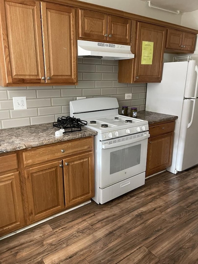 kitchen featuring white appliances, dark hardwood / wood-style floors, decorative backsplash, and dark stone countertops