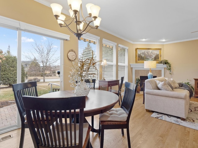 dining room featuring crown molding, a notable chandelier, a fireplace, and light hardwood / wood-style flooring