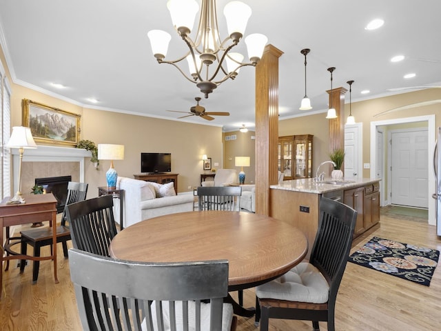 dining area with crown molding, a tiled fireplace, sink, and light wood-type flooring