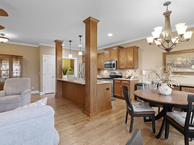 kitchen with appliances with stainless steel finishes, backsplash, decorative columns, decorative light fixtures, and light wood-type flooring