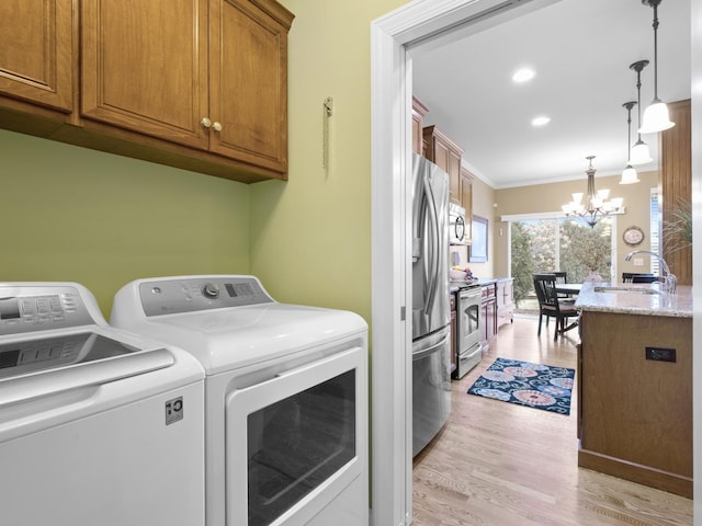 laundry area featuring sink, light wood-type flooring, cabinets, a notable chandelier, and washer and clothes dryer