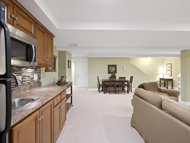 kitchen featuring black fridge, decorative backsplash, sink, and light carpet