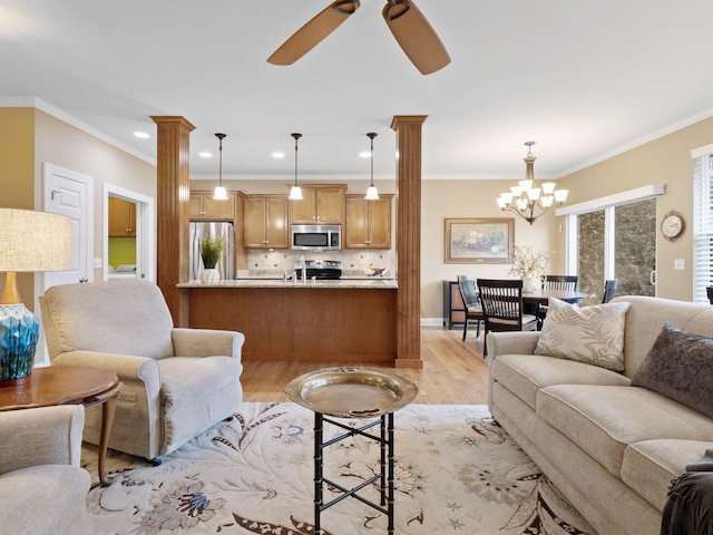 living room featuring decorative columns, ornamental molding, ceiling fan with notable chandelier, and light wood-type flooring